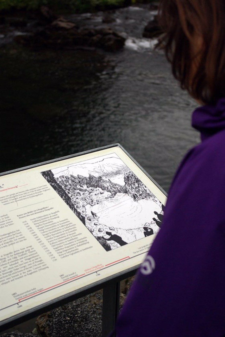 Tourist reading a sign at Drekkingahylur (drowning pond)